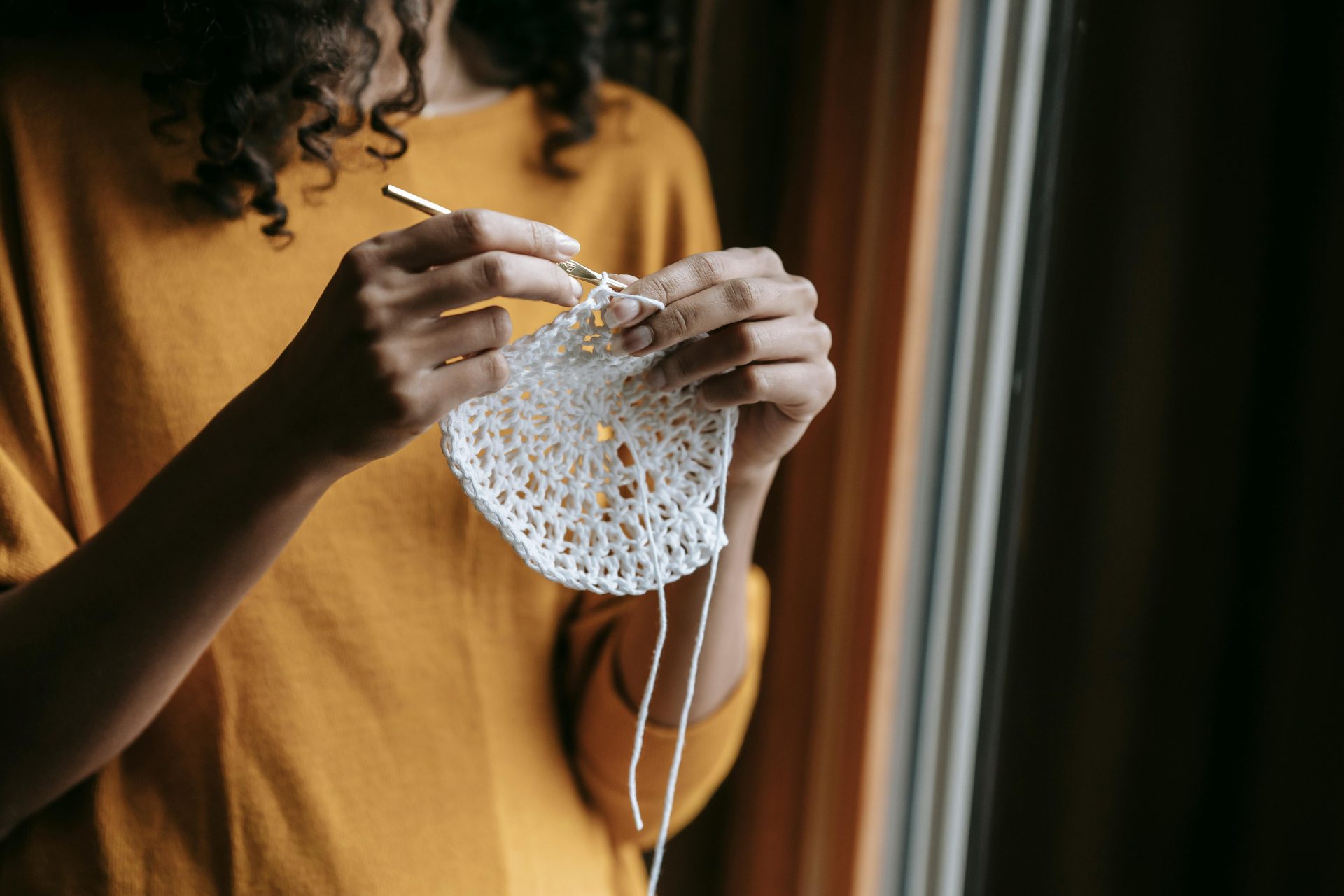 Woman crocheting with white yarn, showcasing handmade artistry indoors.